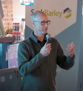 a man holding a microphone speaking at a SaskBarley event